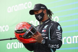 Pebalap Mercedes, Lewis Hamilton, saat memegang helm kemenangan Michael Schumacher. Dia meraih helm tersebut setelah menyamai rekor kemenangan Schumacher. (Foto: AFP/BRYN LENNON via kompas.com)