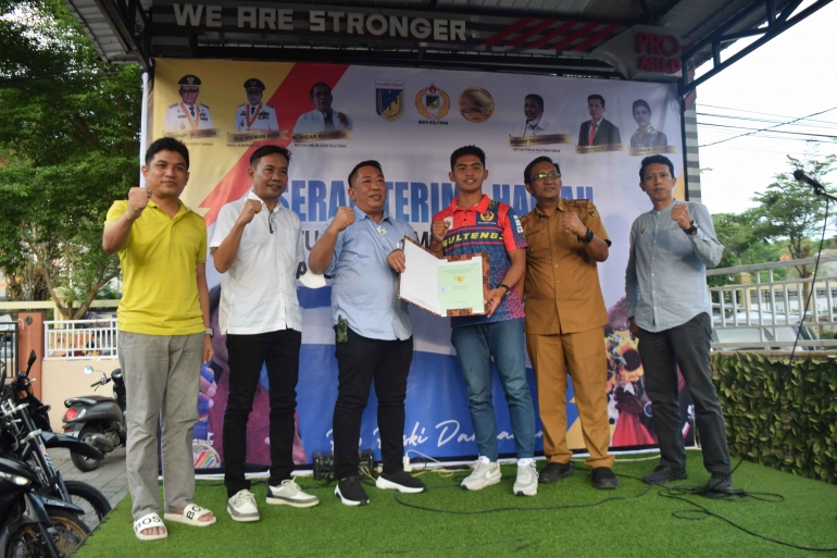 Ketua Umum KONI Sulteng menyerahkan sertifikat rumah Rio Riski Darmawan, atas prestasi Rio mendapatkan medali Emas SEA Games 2021 Vietnam. 