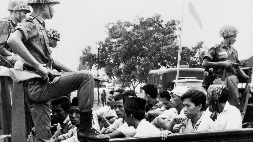 Foto diambil pada 30 Oktober 1965, sebulan setelah kudeta yang gagal oleh Partai Komunis Indonesia. Tentara berjaga di atas truk yang mengangkut tahanan aktivis Pemuda Rakyat. AP Photo