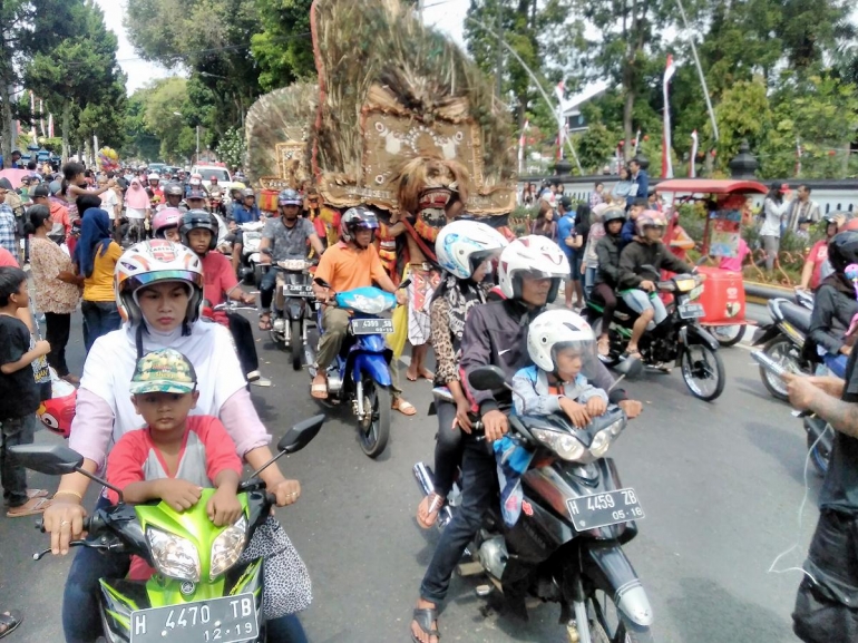 Foto oleh Meilana Lestari. Peserta karnaval bercampur dengan pengendara kendaraan, pedagang keliling, dan warga kota.