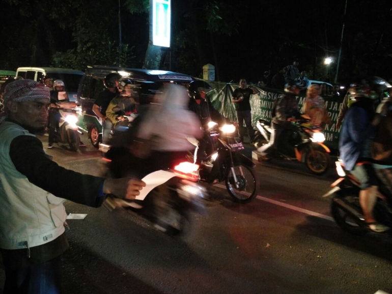 Anggota ormas yang sedang membawa brosur untuk dibagikan kepada pengendara yang lewat. Sementara di seberangnya adalah anggota ormas yang berdiri membawa spanduk unjuk rasa (dokpri)
