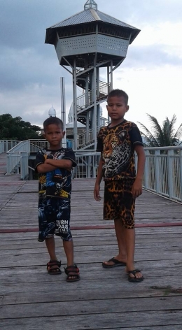 Dua orang anak sedang berpose dengan latar Menara Pandang ke Pantai Ulee Lheu (foto dok pri).