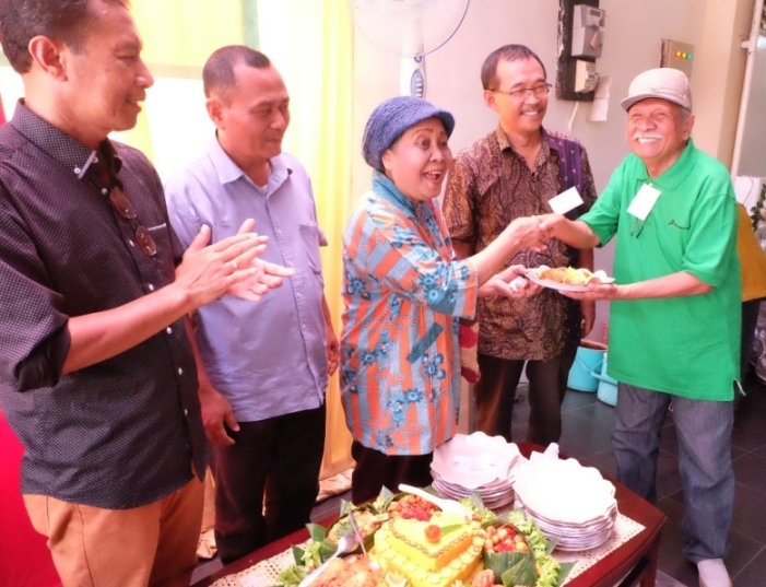 Dra Andarini, dosen senior AWS/Stikosa menyerahkan potongan tumpeng untuk wartawan senior Peter A. Rohi -Foto ABH