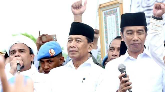 Jokowi (paling kanan, memegang mik sambil tersenyum), Habieb Rizieq paling kiri (sedang berbicara dengan mik) dalam suatu moment Aksi 212 beberapa waktu lalu. || Sumber gambar: katadata.co.id