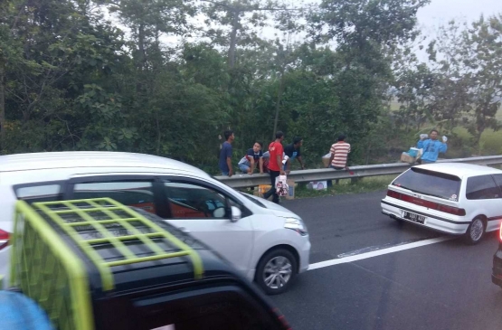 Warga sepanjang Pantura menjajakan dagangan di pinggir jalan tol Trans Jawa. Ini bagian dari upaya warga setempat untuk meraih nilai ekonomi dari tol tersebut, tapi dilakukan secara serampangan. Ini membahayakan keselamatan mereka, juga berbahaya bagi pengendara. Stakeholder yang relevan dengan jalan tol Trans Jawa, hendaknya mengelola hal ini, agar jalan tol berkontribusi langsung pada ekonomi rakyat setempat. Foto: isson khairul