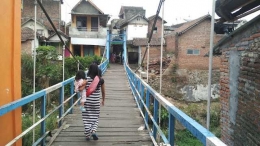 Seorang ibu yang menggendong anaknya sedang meniti jembatan gantung yang berdiri di atas Sungai Brantas. Jika tak punya nyali, jangan coba-coba menaiki kendaraan bermotor di sini.|Dokumentasi pribadi