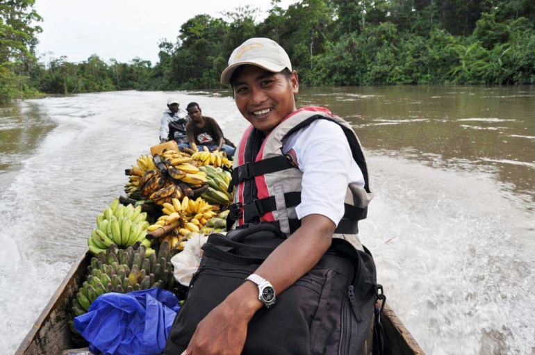 Bruder Gregorius Sigit Wiyono SCJ (38) berada di atas perahu motor berbahan bakar bensin. Ia dalam perjalanan pulang dari stasi menuju Paroki Maria Bintang Laut di Kokonao, Mimika, Papua. Tampak banyak pisang sebagai oleh-oleh yang diberikan umat sebagai ganti persembahan uang. (Dok Pribadi)