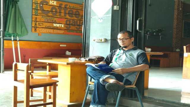 Pak Jamhuri memanfaatkan waktu senggang untuk membaca buku di kedai kopinya, Skala Banda Aceh (Foto: dokumen pribadi)