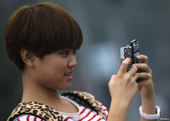 Ilustrasi: Seorang remaja perempuan memegang dua ponsel saat berfoto di pusat kota Shanghai, 22 Oktober 2012 (Sumber: VOA Indonesia/Reuters)