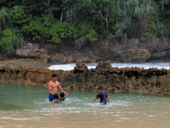 Keluarga kecil yang bermain di kolam alami yang terhalang dinding batuan karang - Dokumentasi Pribadi