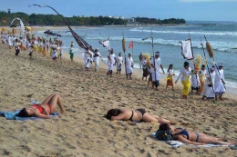 Wisatawan mancanegara hanya memakai kutang dan cawat berjemur di pasir Pantai Kuta, Bali, tanpa jadi tontontan bahkan ketika ada upacara adat setempat (Sumber: kabar24.bisnis.com)