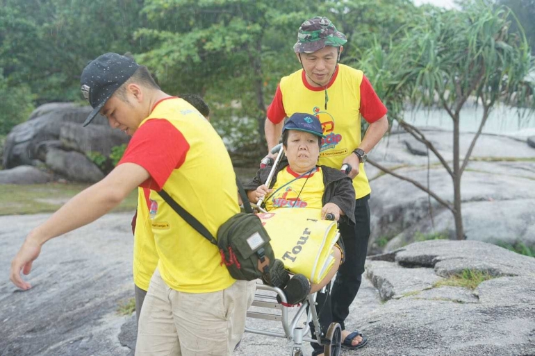 Seorang pengguna kursi roda bersama wisatawan non-disabilitas tengah menyusuri bebatuan di Pantai Penyabong, Desa Batu Lubang Padang Kandis, Membalong. Foto: Dok. Permata Tour Belitung & CIP CIP Community