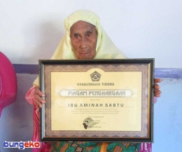 Almh. Amina Sabtu menunjukkan piagam penghargaan yang diberikan oleh Kesultanan Tidore padanya usai upacara 18 Agustus 2017. Inilah satu-satunya penghargaan yang pernah beliau terima atas keberanian yang dilakukan 72 tahun lalu. FOTO: Eko Nurhuda