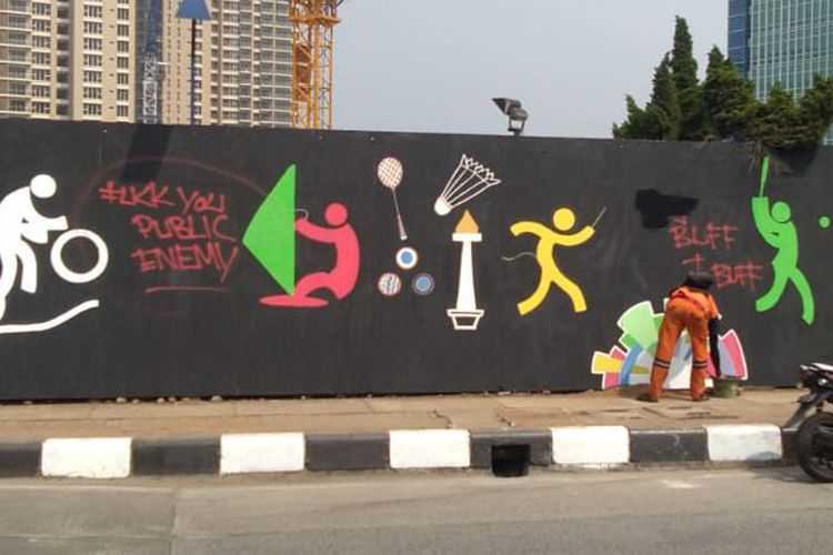 Petugas penanganan prasarana dan sarana umum (PPSU) Kelurahan Pondok Pinang membersihkan coretan-coretan yang mengotori mural Asian Games 2018 di perempatan Pondok Indah Mall, Jakarta Selatan, Rabu (25/7/2018). Gambar dan keterangan gambar dari KOMPAS.com/NURSITA SARI