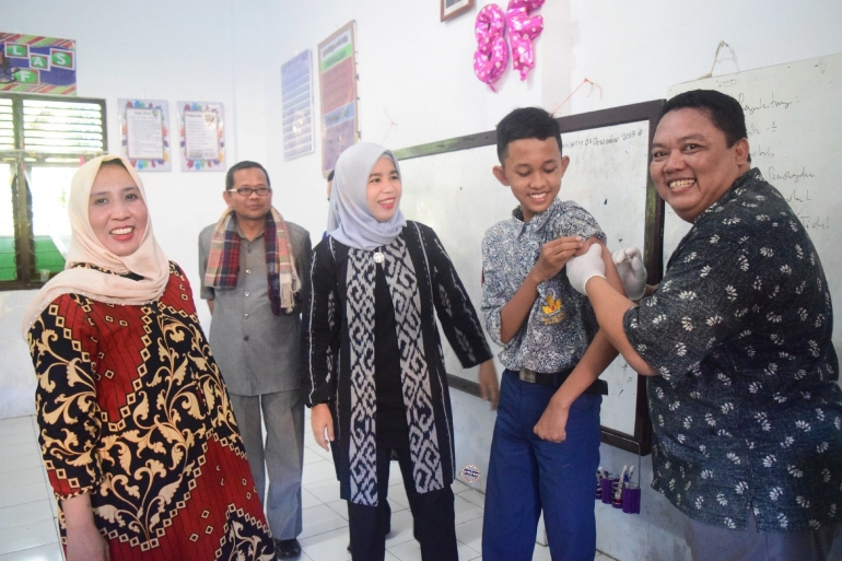 Sri Dewi Yanti (tengah) bantu memegangi siswa untuk divaksinasi MR (06/12/2018).