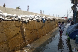 Warga melewati genangan air dari rembesan air laut yang menembus tanggul karung pasir di Muara Baru (kompas.com)
