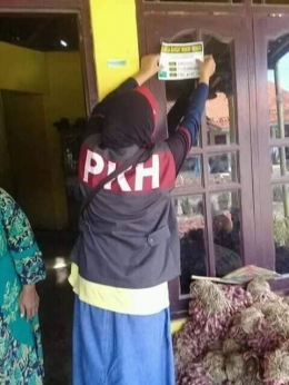 petugas pendamping PKH sedang menempelkan sticker Keluarga Miskin (sumber foto: akun Facebook Qonitah Zahirah Humaira)