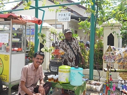 Dua seniman dan budayawan Kebumen yang tengah mengikuti Kirab Budaya Cap Go Meh 2019. Slamet Esser (berbaju batik) tengah memegang salah satu tokoh wayang kartun yang di sebelah kanannya nampak sederet barang dagangannya di depan Kantor Camat Kebumen. Dokumen Pribadi. 