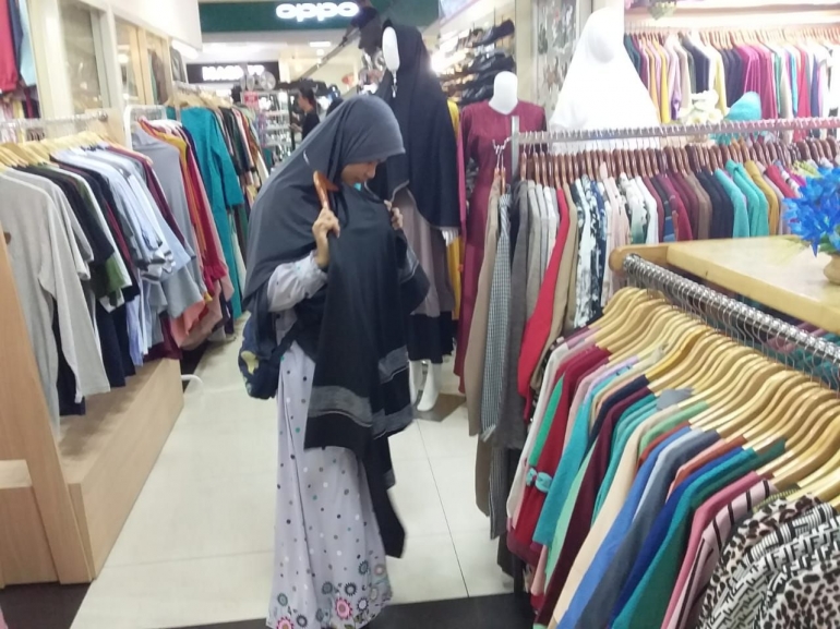 Annisa (pembeli) sedang memilih koleksi pakaian toko 