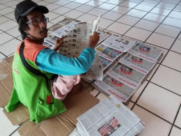 Si Abang Koran menggelar koran di lantai Terminal Kampung Rambutan. Foto | Dokpri