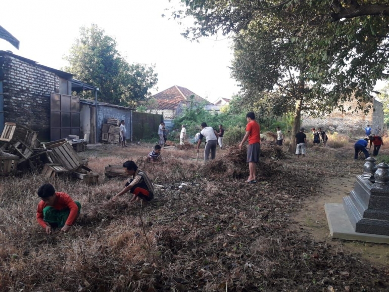 Warga saat membersihkan rumput di areal pemakaman setempat