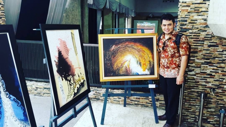 Ali froghi dengan karya lukisnya dalam sebuah pameran di Makassar (Instagram @AliFroghi)
