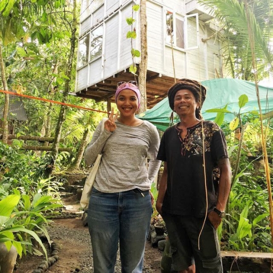 Hartono bersama salah seorang tamu, berfoto dengan latar belakang rumah pohon yang merupakan tempat tinggalnya bersama istrinya. Sumber: Hartono Lokodjoyo