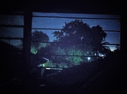 Jendela kamar dengan view waktu malam. Bagian terang di sebelah kanan atas adalah langit Jakarta. Tepat di bawah jendela ada pagar tembok pembatas dan saluran air hujan yang menjadi jalan perlintasan musang di malam hari (dokumentasi pribadi).