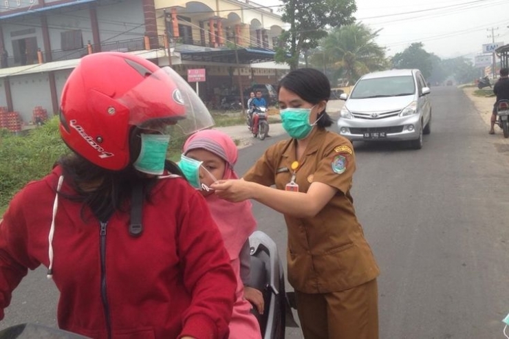 Seorang aparatur sipil negara (ASN) Dinas Kesehatan memasangkan masker kepada anak dan ibunya di Kecamatan Ngabang, Kabupaten Landak, Kalimantan Barat, Senin (9/9/2019).(Kompas/dok. Pemkab Landak)