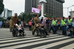 Gubernur DKI Jakarta Anies Baswedan mendorong pengguna kursi roda menyebrangi pelican crossing di Halte Bank Indonesia, Selasa (4/9/2018). (KOMPAS.com/JESSI CARINA )