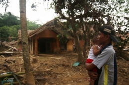 Jahaedi sambil menggendong anaknya berada di depan bekas rumahnya yang hancur akibat banjir bandang di Kampung Seupang, Pajagan, Sajira, Lebak, Sabtu (15/2). (ACTNews/Eko Ramdani) 