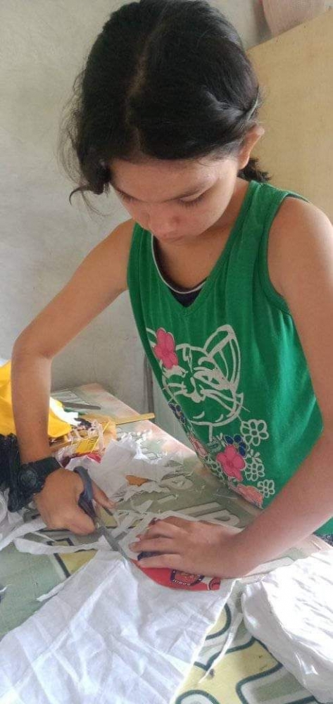 (Putri Sophia Hebi sedang membantu ibunya menjahit masker untuk warga)