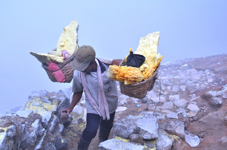 Belerang adalah salah satu anugerah sumber daya alam Indonesia yang melimpah. Foto ini adalah tentang endapan belerang berasal dari pusat-pusat sisa aktivitas vulkanisma berupa solfatara dan fomarola yang berada di bagian tepi danau Kawah Ijen. Tampak para penambang mengangkut secara manual ke lokasi penampungan di Kawasan Kawah Ijen di Kabupaten Banyuwangi, Jawa Timur (Sumber: Dok. Pribadi Andi Setyo Pambudi)