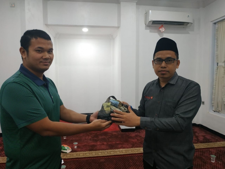 M. Fadhil (kiri) menyerahkan uang kotak infak anak yatim ke Idham Fadhil untuk selajutnya diserahkan ke panti asuhan. (foto humas setdakab padang pariaman)