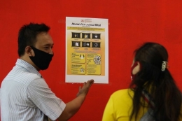 Pegawai swalayan Carrefour menunjukkan poster kepada pengunjung usai ditempel di BG Junction, Surabaya, Jawa Timur, Rabu (27/5/2020). Penempelan poster yang berbunyi Aturan New Normal Ritel itu agar pengunjung memahami protokol pencegahan penularan COVID-19 saat mengunjungi pusat perbelanjaan. Sumber: KOMPAS.com/ANTARA FOTO/Didik Suhartono