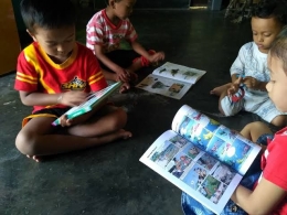 Anak-anak asyik melihat gambar pada buku bergambar. Ini termasuk cara membaca bagi anak TK atau awal SD. Membaca gambar. Ilustrasi: www.bintangbrilliant.co.id
