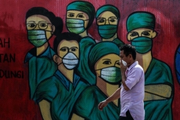 ilustrasi: Warga menggunakan masker saat melintas di depan mural tentang pandemi virus corona atau COVID-19 di Jalan Raya Jakarta-Bogor, Depok, Jawa Barat, Selasa (7/4/2020). Mural tersebut ditujukan sebagai bentuk dukungan kepada tenaga medis yang menjadi garda terdepan dalam menghadapi COVID-19 di Indonesia. (Foto: KOMPAS.com/GARRY LOTULUNG)