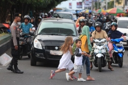Salah seorang anggota Polisi memberhentikan kendaraan di depan pasar Higienis Ternate agar tiga bocah menyebrang jalan, (12/6/2018) Dokpri.