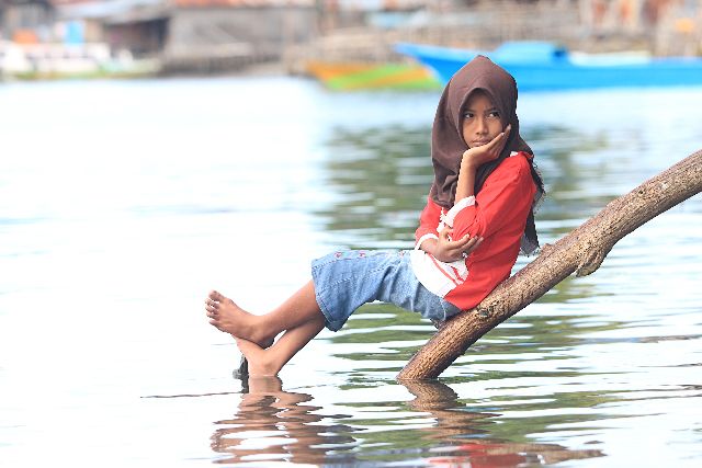 Seorang anak duduk menyendiri memanfaatkan sebatang kayu di atas air. Dokpri