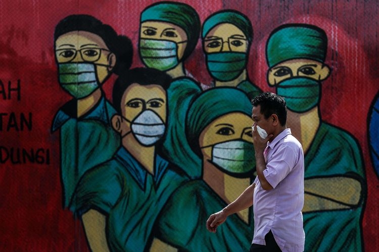 Ilustrasi: Warga menggunakan masker saat melintas di depan mural tentang pandemi virus corona atau COVID-19 di Jalan Raya Jakarta-Bogor, Depok, Jawa Barat, Selasa (7/4/2020). Mural tersebut ditujukan sebagai bentuk dukungan kepada tenaga medis yang menjadi garda terdepan dalam menghadapi COVID-19 di Indonesia. (Sumber: KOMPAS.com/GARRY LOTULUNG)