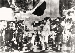 Sukarno pawai bersama tentara Jepang dengan membawa bendera merah putih dan bendera Jepang, semuanya berdiri sejajar. foto milik javapost.nl