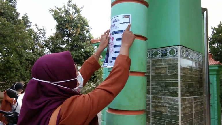 Mahasiswa KKN Unikama menempelkan poster di salah satu masjid Desa Ngorogunung | dokpri