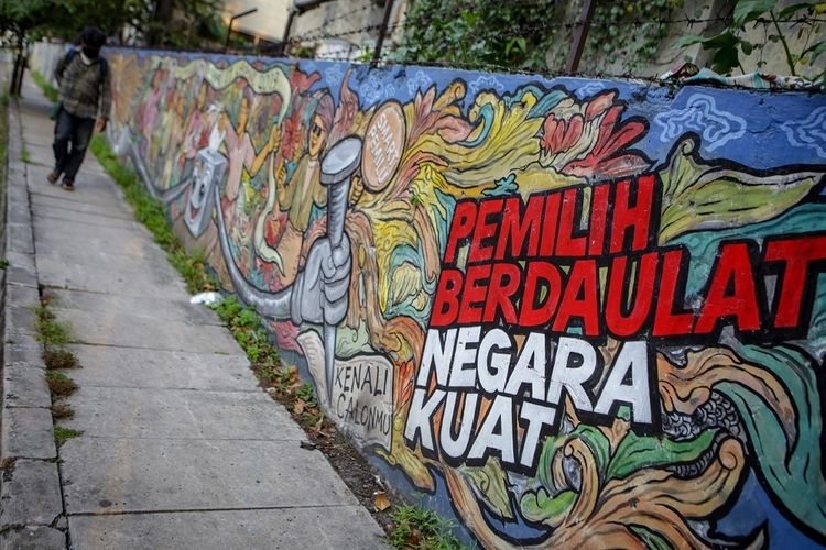  Warga melintas di depan mural bertema pemilihan umum di kawasan Pasar Anyar, Kota Tangerang, Banten, Kamis (7/5/2020). Presiden Joko Widodo menunda pemungutan suara Pemilihan Kepala Daerah (Pilkada) 2020 hingga Desember 2020 akibat wabah COVID-19. ANTARA FOTO/Fauzan/aww.(ANTARA FOTO/FAUZAN via KOMPAS.com))