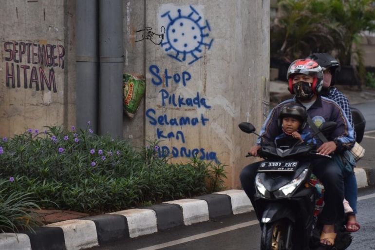 Grafiti yang berisi harapan masyarakat terkait penundaan Pilkada 2020 karena pandemi Covid-19 menghiasi tiang penyangga jalan layang bus transjakarta di Jalan Cildug Raya, Kebayoran Lama, Jakarta, Sabtu (3/10/2020). (KOMPAS/WAWAN H PRABOWO)