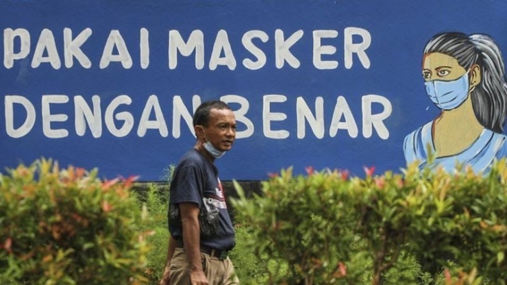 Warga berjalan di depan mural dengan tema COVID-19 di halaman Balai Kota Depok, Depok, Jawa Barat, Rabu (06/01). Sumber : bbc.com