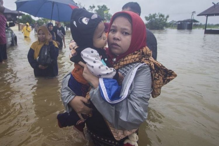 Warga menggendong anaknya melintasi banjir di Desa Kampung Melayu, Kabupaten Banjar, Kalimantan Selatan, Jumat (15/01). Banjir ini digambarkan sebagai banjir terbesar yang melanda provinsi tersebut.(Antara Foto via KOMPAS.com)