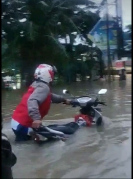 Seorang pengendara motor nekad melintas di genangan banjir. Pengendara harus mendorong motor bila nekad melintas. Gambar: foto dari karyawan/Kharis