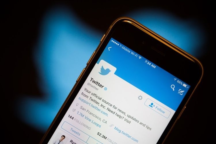 Ilustrasi Aplikasi Twitter di ponsel di depan logo Twitter| Sumber: Bloomberg via Kompas.com