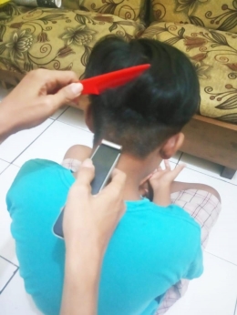 Anakku sedang kupotong rambutnya di depan sofa yang sudah kuperbaiki (Foto : Mahendra Paripurna)