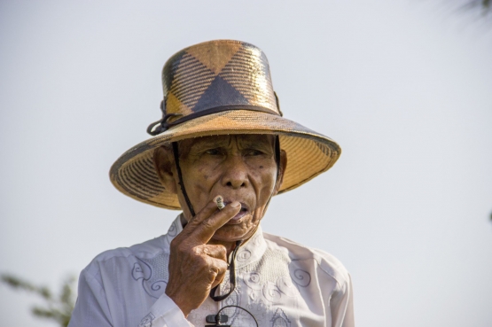Seorang pria tua (mbah, dalam bahasa Jawa) sedang menghisap sebatang rokok | bolehmerokok.com